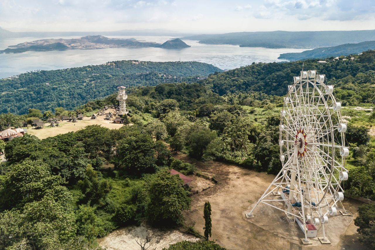 Aerial of Tagaytay Picnic Grove - A large ferris wheel, a park and Taal volcano and lake in the background.